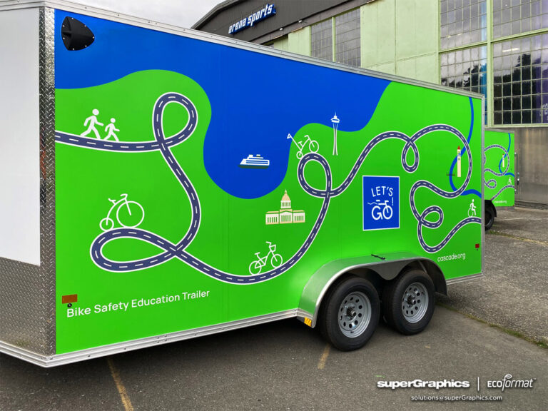 Side view of a bike safety education trailer with green and blue graphics, including a map and cycling symbols, from Cascade Bicycle Club