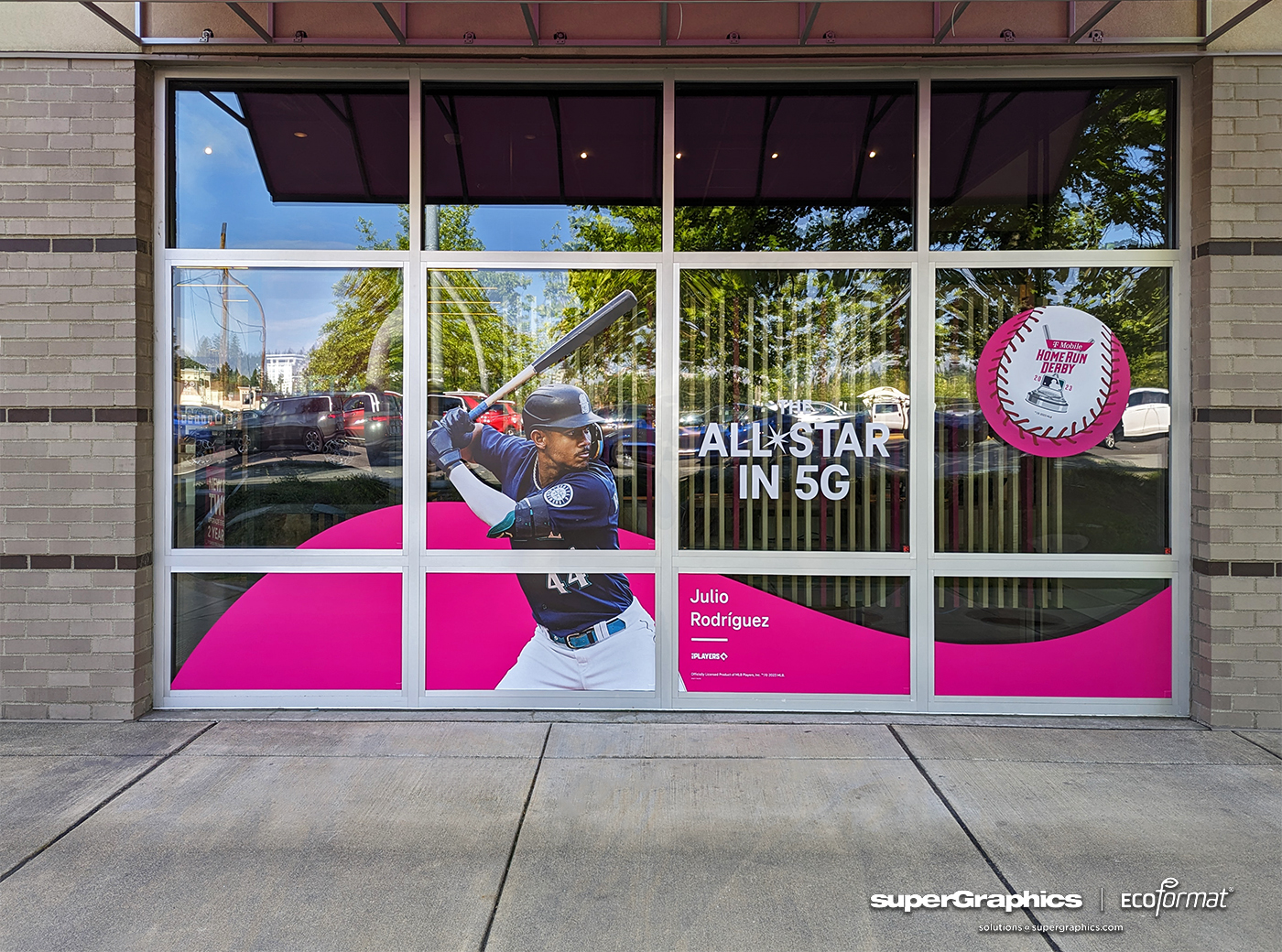 T-Mobile store windows from a side angle, featuring promotional graphics for 'ALLSTAR in 5G' with the image of Julio Rodriguez, a baseball icon, against a vivid pink backdrop.