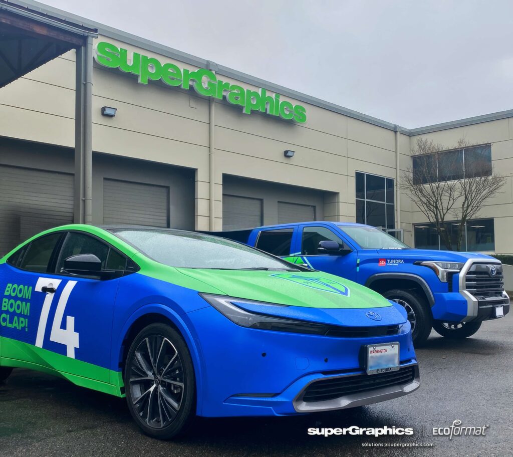 Blue and green vinyl-wrapped Prius with '74' and 'BOOM BOOM CLAP!' text, part of a Seattle fleet rebranding campaign.