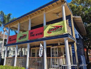 A blue two-story building with large banners promoting Brooks Hyperion House and the slogan "Believe the Hype."