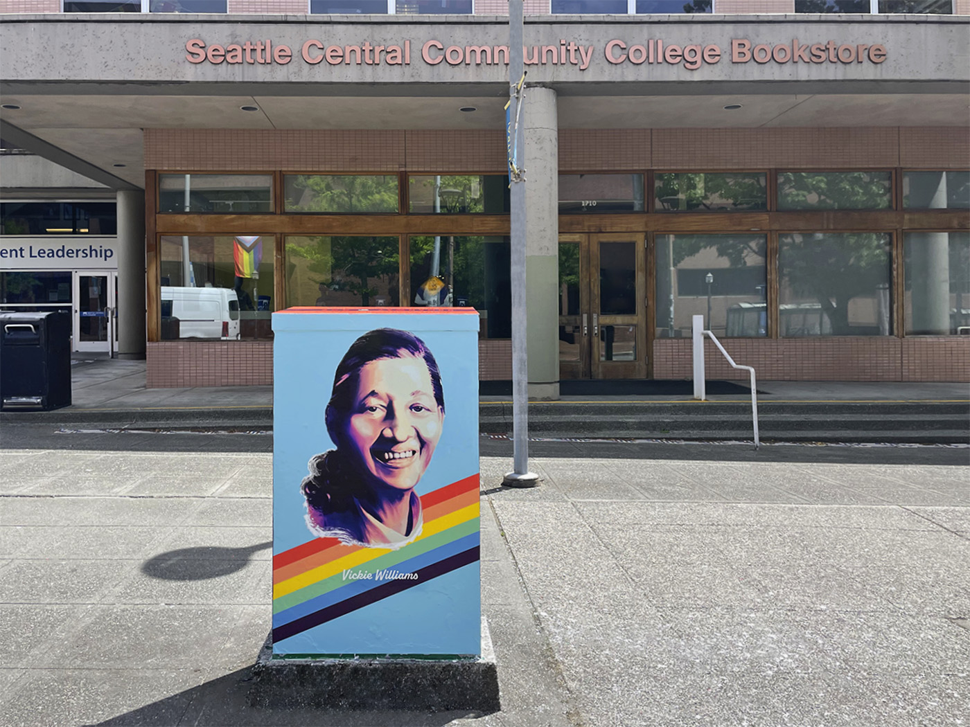 Utility box wrap featuring a portrait of a smiling woman with a rainbow stripe, located in front of Seattle Central Community College Bookstore in Seattle, WA