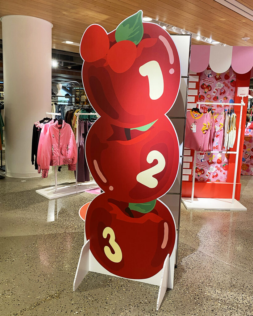 Nordstrom Hello Kitty Anniversary freestanding signage, produced and installed by SuperGraphics. Showcases apple graphic on freestanding signage inside of Nordstrom pop-up.