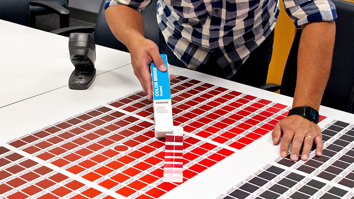 Color matching, completed by SuperGraphics. Showcases SuperGraphics employee matching color swatches to Pantone color book.