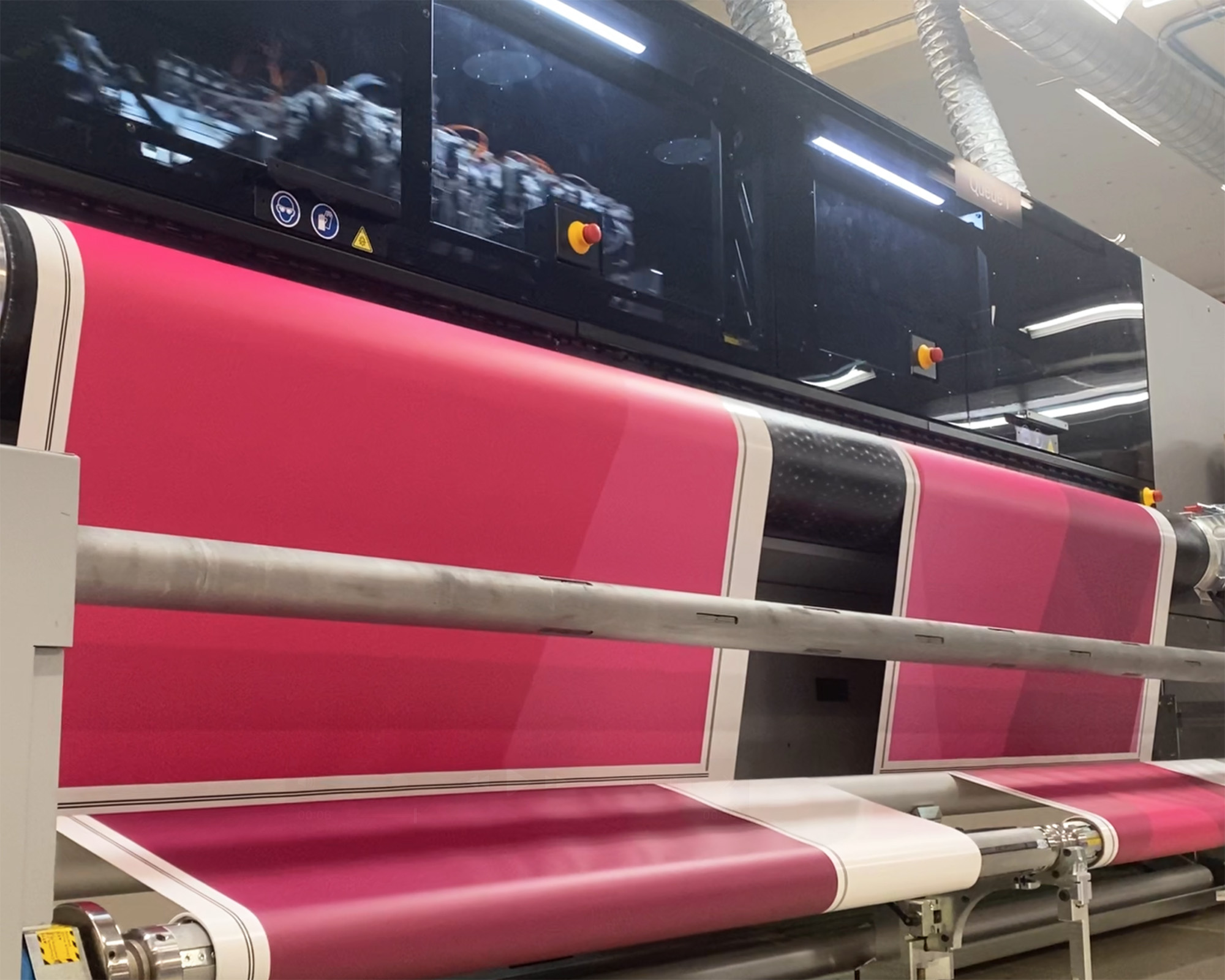 Photo of large format printing at SuperGraphics. Showcases roll presses printing magenta graphic at scale.