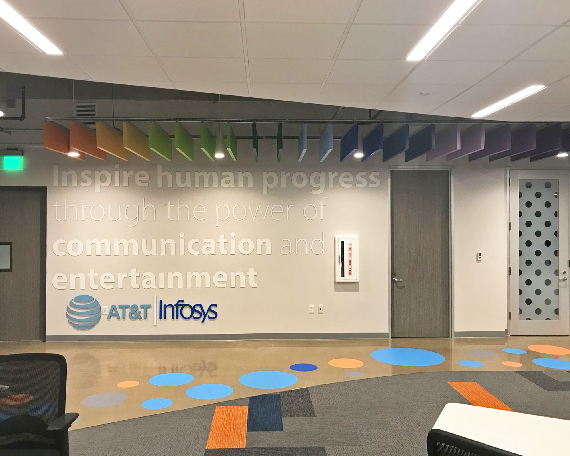 Mission wall graphic with dimensional AT&T and Infosys co-branding logos, featuring a large white vinyl mission statement and rainbow ceiling installation.