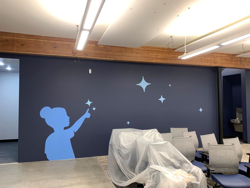 Photo of completed wall mural on a construction site, produced and installed by SuperGraphics. Showcases graphic of young girl pointing at stars.