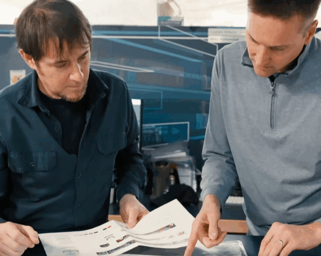Two SuperGraphics team members reviewing physical color proofs and print details in the production facility to ensure brand-obsessed quality.
