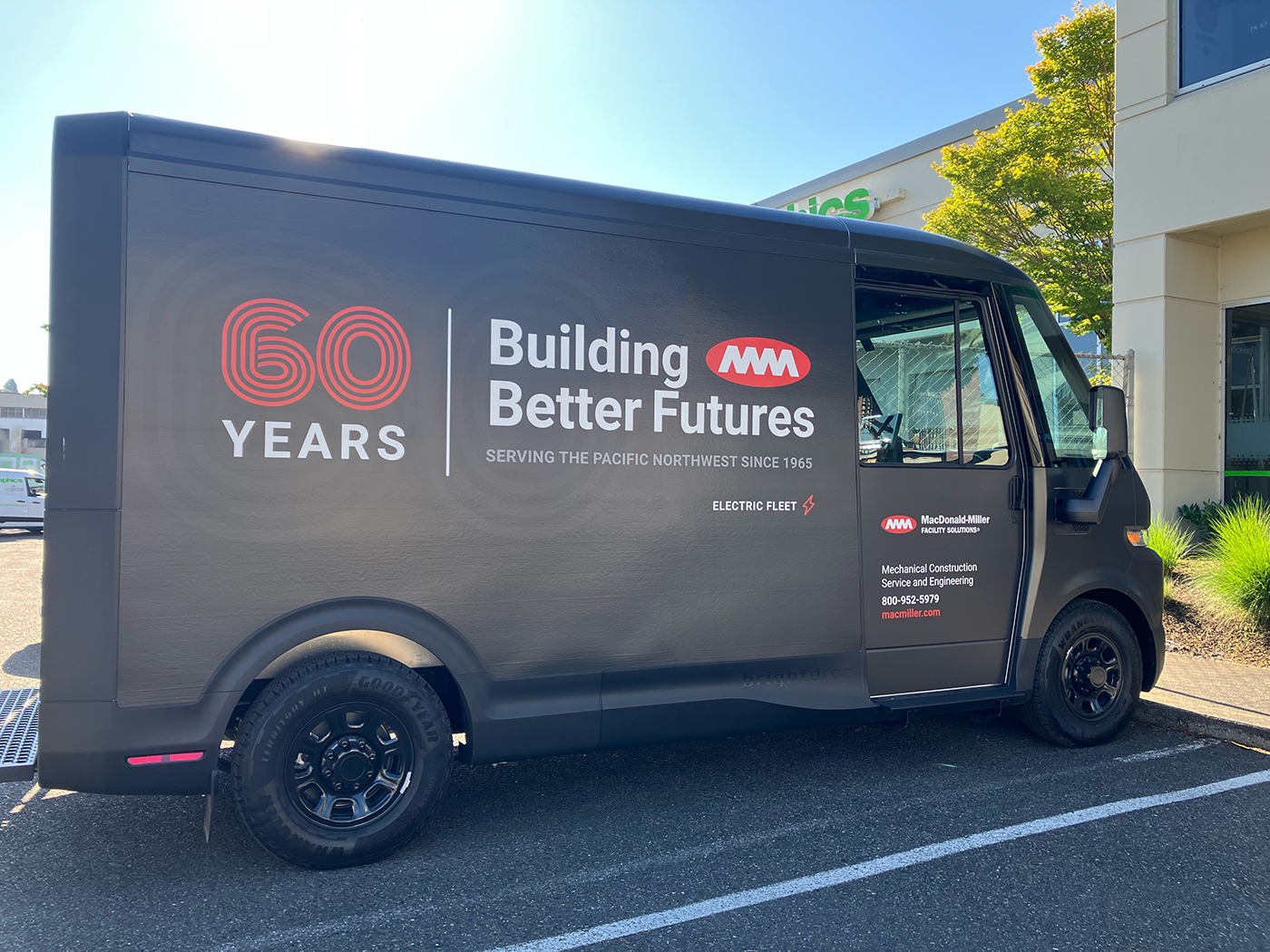 MacDonald-Miller electric fleet van wrap on a matte black finish celebrating '60 YEARS' with corporate branding and 'Building Better Futures' message.