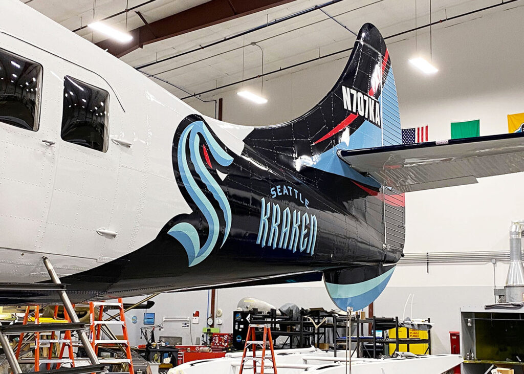 Vinyl graphic wrap of the Seattle Kraken team logo and text applied to the tail section of an aircraft in a hangar.