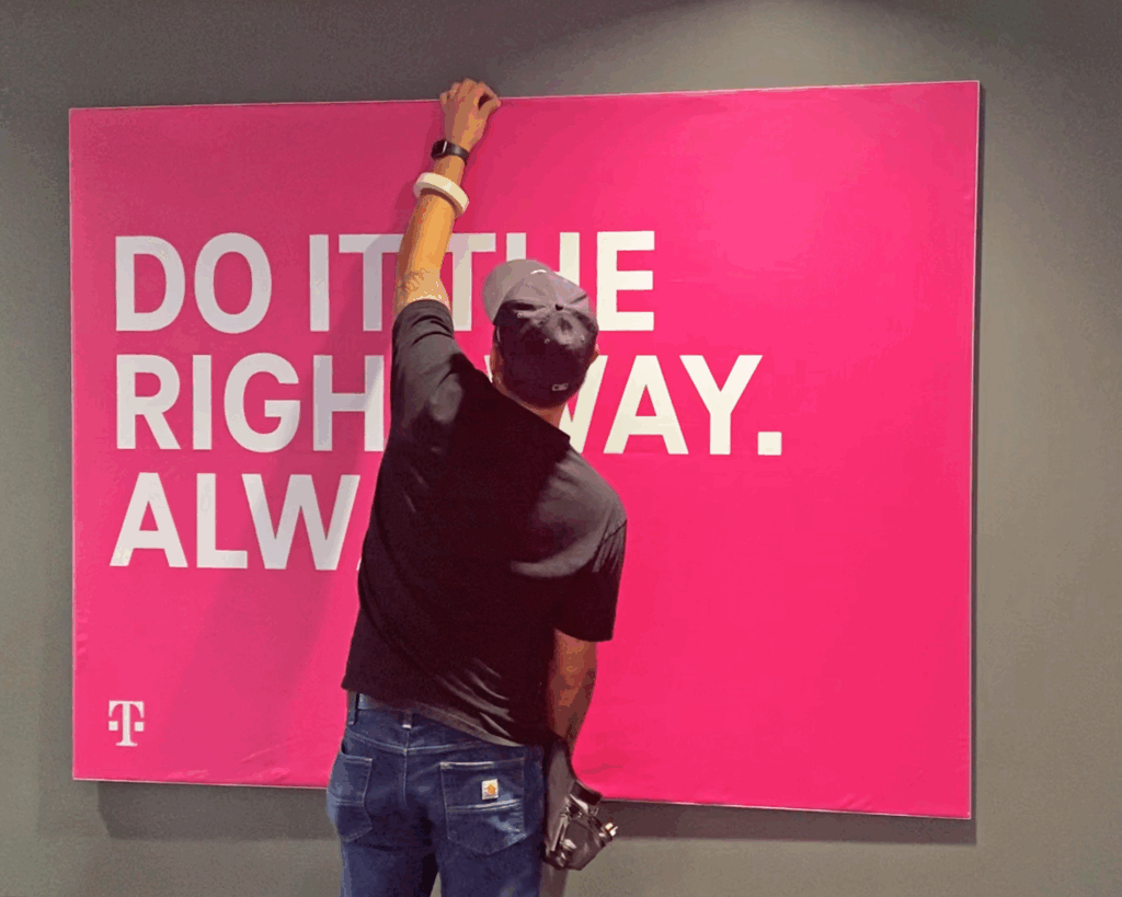 Photo of graphic installer from SuperGraphics holding SEG Frame, produced by SuperGraphics. The SEG Frame Graphic states "Do it right, always," in front of magenta.