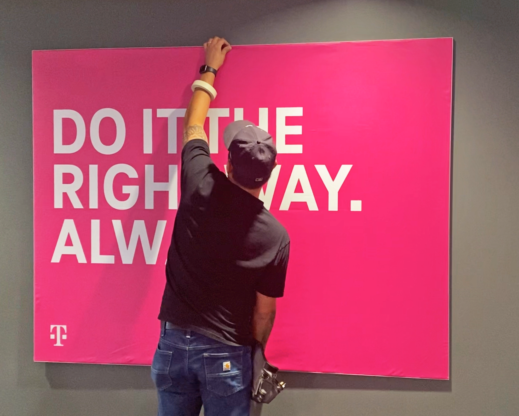 Photo of graphic installer from SuperGraphics holding SEG Frame, produced by SuperGraphics. The SEG Frame Graphic states "Do it right, always," in front of magenta.