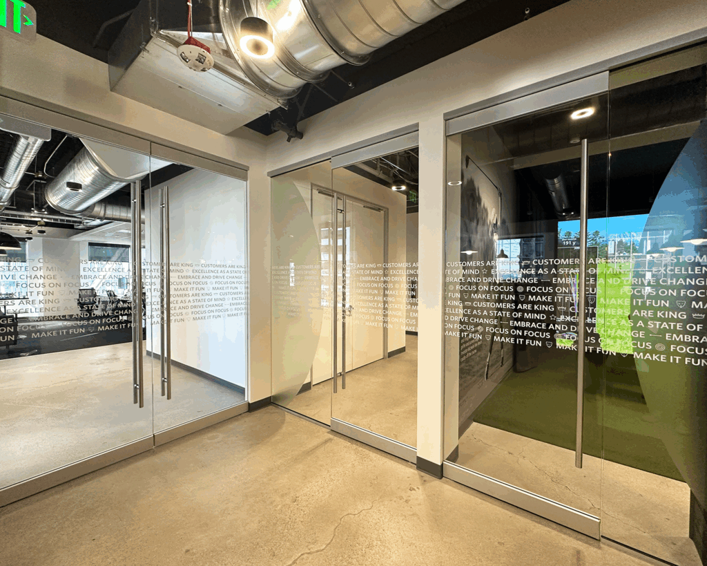 White printed privacy film on glass office doors with corporate mission statement text.