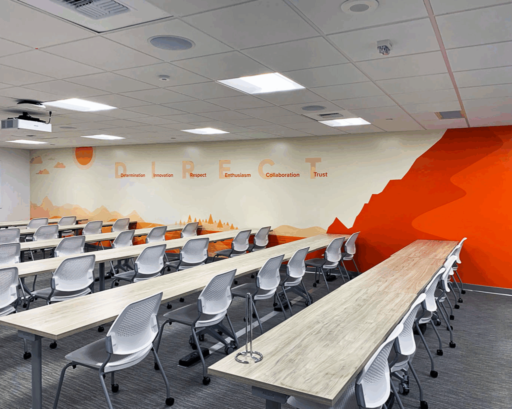 Large wall graphic in a corporate training room featuring company values like 'DETERMINATION' and a sunset landscape design with orange gradients.