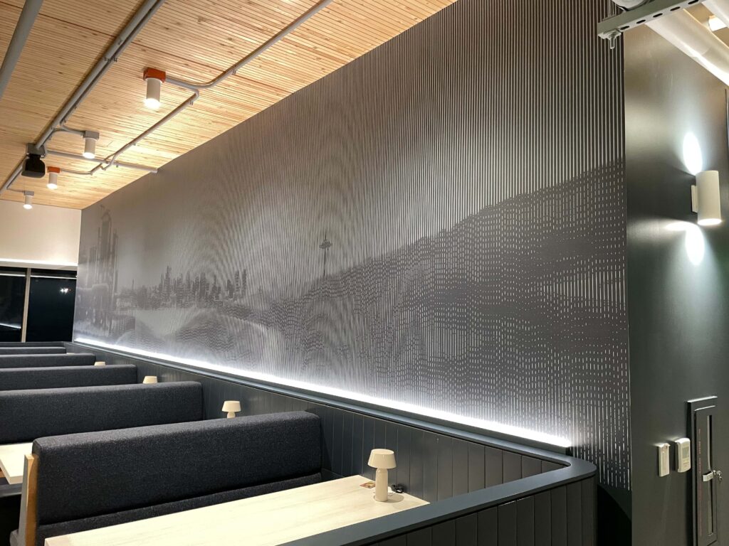 Monochromatic wall mural with a linear Seattle cityscape pattern installed above booth seating in a modern office dining area.