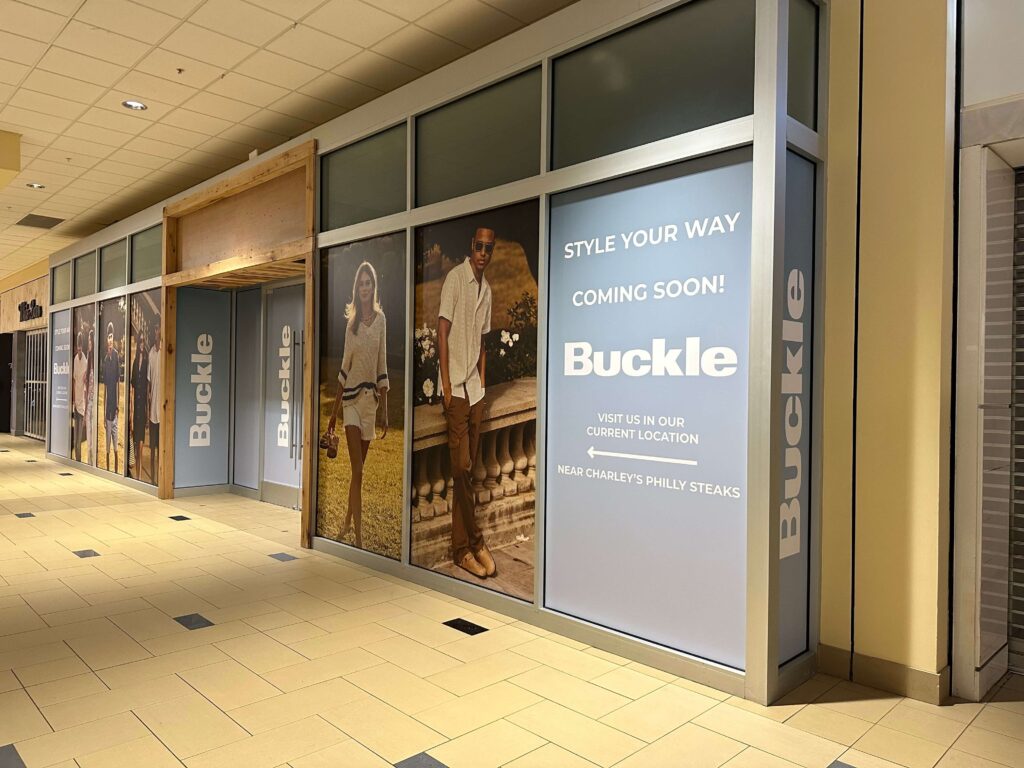 Buckle mall storefront barricade with full-height lifestyle graphics and branded “Style Your Way — Coming Soon!” messaging, produced and installed by SuperGraphics.