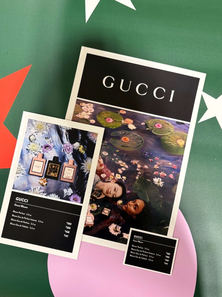 Printed Gucci beauty display signs produced by SuperGraphics for a major retailer, featuring floral campaign imagery and product pricing panels.