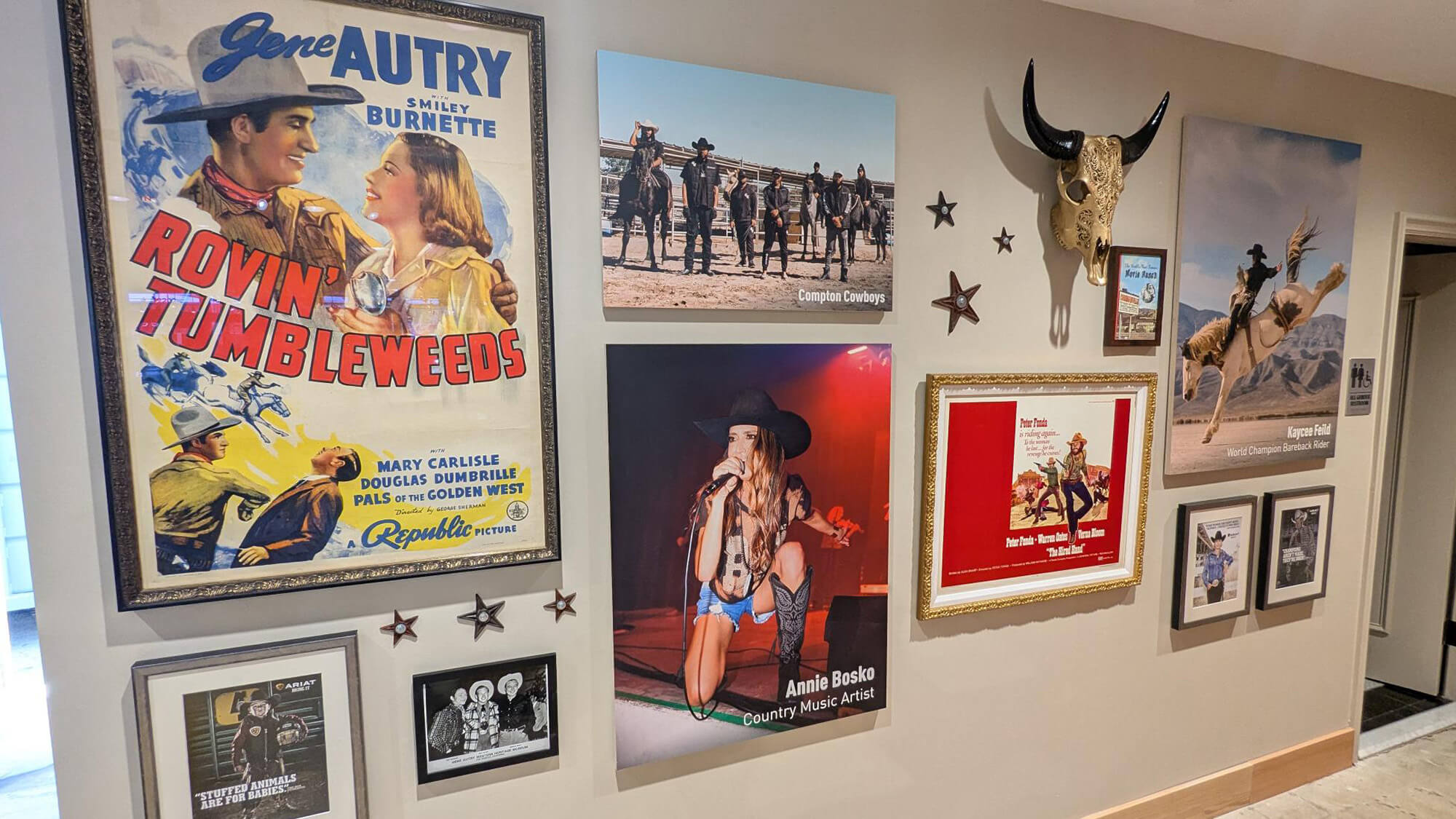 Ariat International interior wall display featuring framed Western artwork, rodeo photography, vintage posters, and a mounted longhorn skull as part of a heritage-inspired retail design.