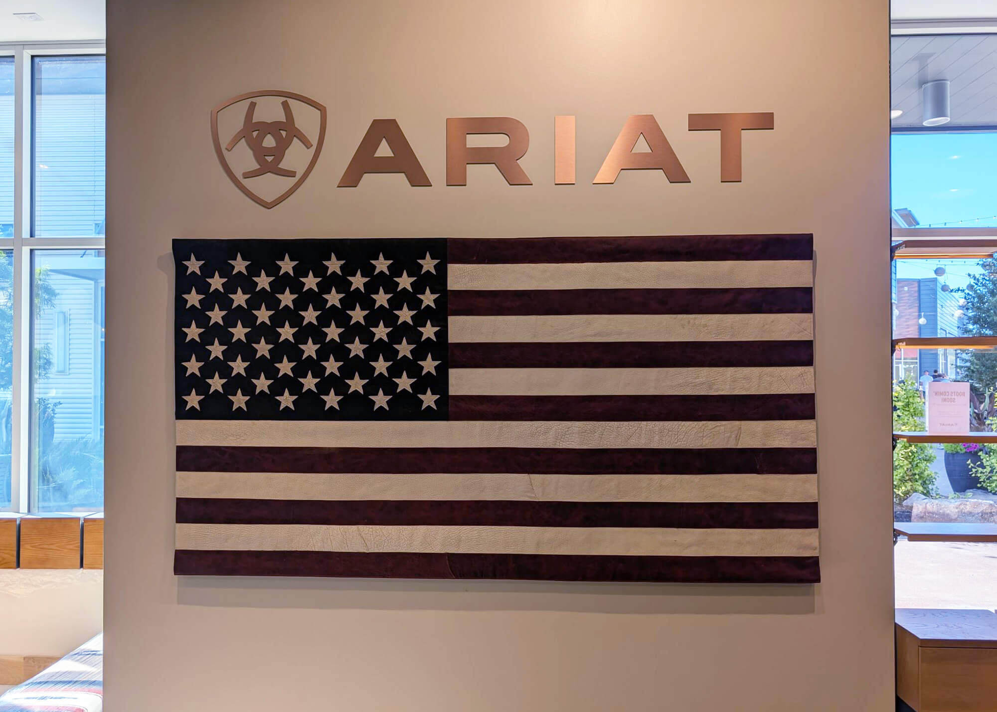 Ariat International interior wall featuring dimensional ARIAT logo signage above a large American flag display in a modern retail store environment.