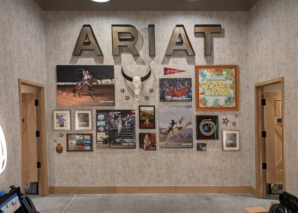 Custom Ariat International interior wall display featuring large metal ARIAT letters, framed rodeo photography, Western memorabilia, and a longhorn skull centerpiece.