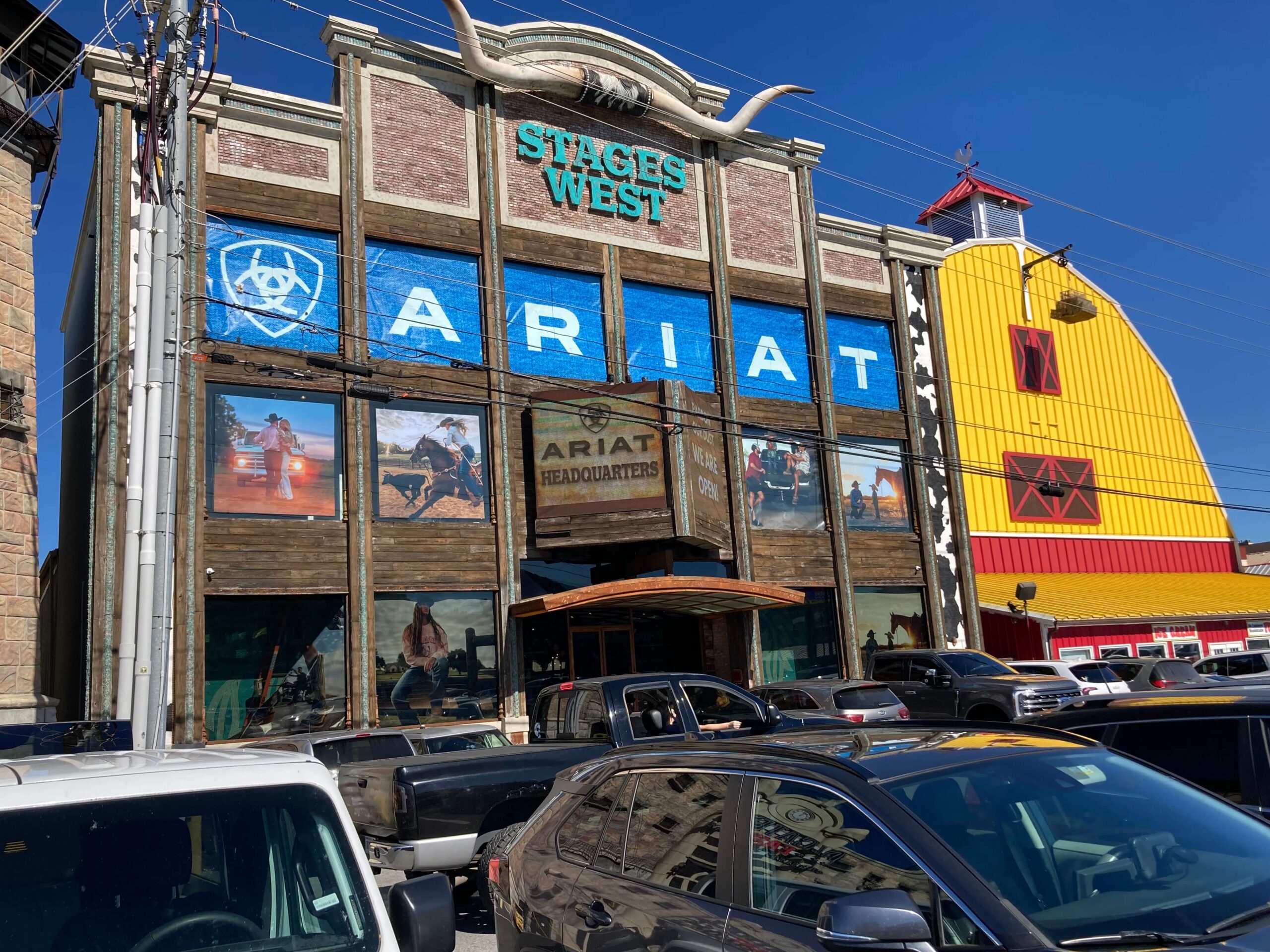 Exterior of Ariat International store featuring large blue ARIAT window graphics, Western lifestyle imagery, and a rustic storefront facade with Stages West signage.