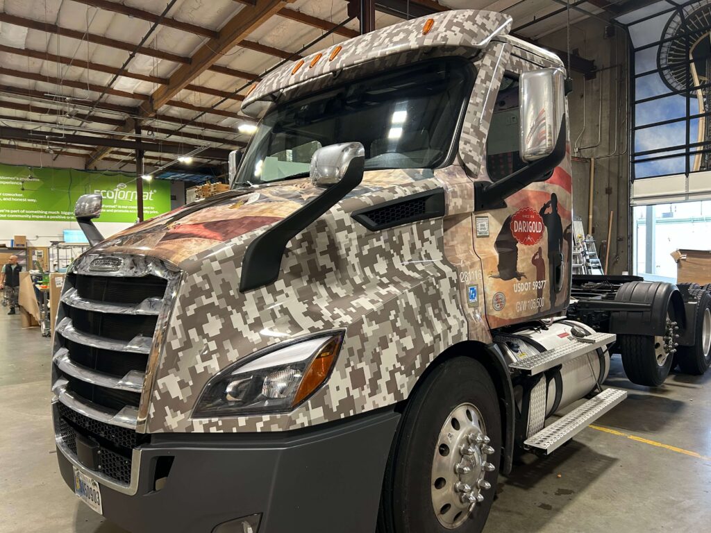 Darigold semi-truck inside the SuperGraphics production facility, wrapped in a custom camouflage fleet graphic with Western imagery and bold door branding.