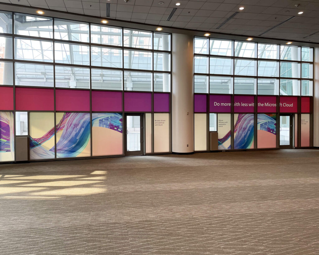 Sustainable large-format branded window graphics produced and installed by SuperGraphics for Microsoft Ignite, featuring colorful abstract designs across a convention center glass facade.