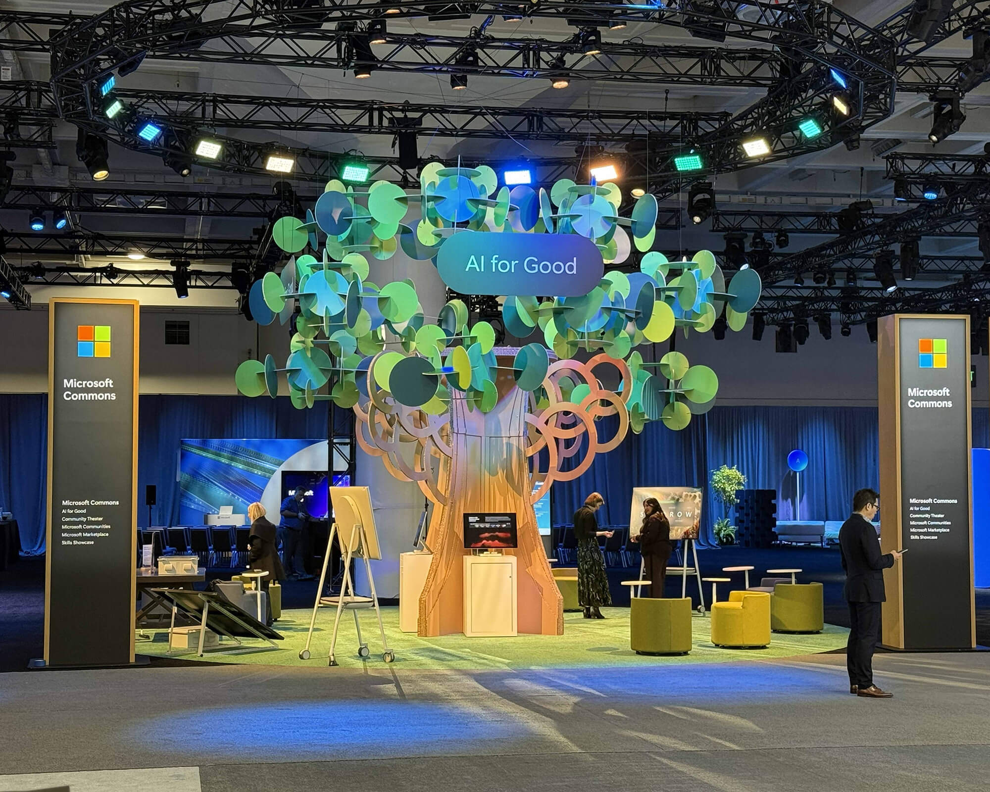 A large recyclable sculptural tree installation produced by SuperGraphics for the AI for Good area within Microsoft Commons at Microsoft Ignite, featuring green and blue circular leaf elements and warm-toned trunk rings.