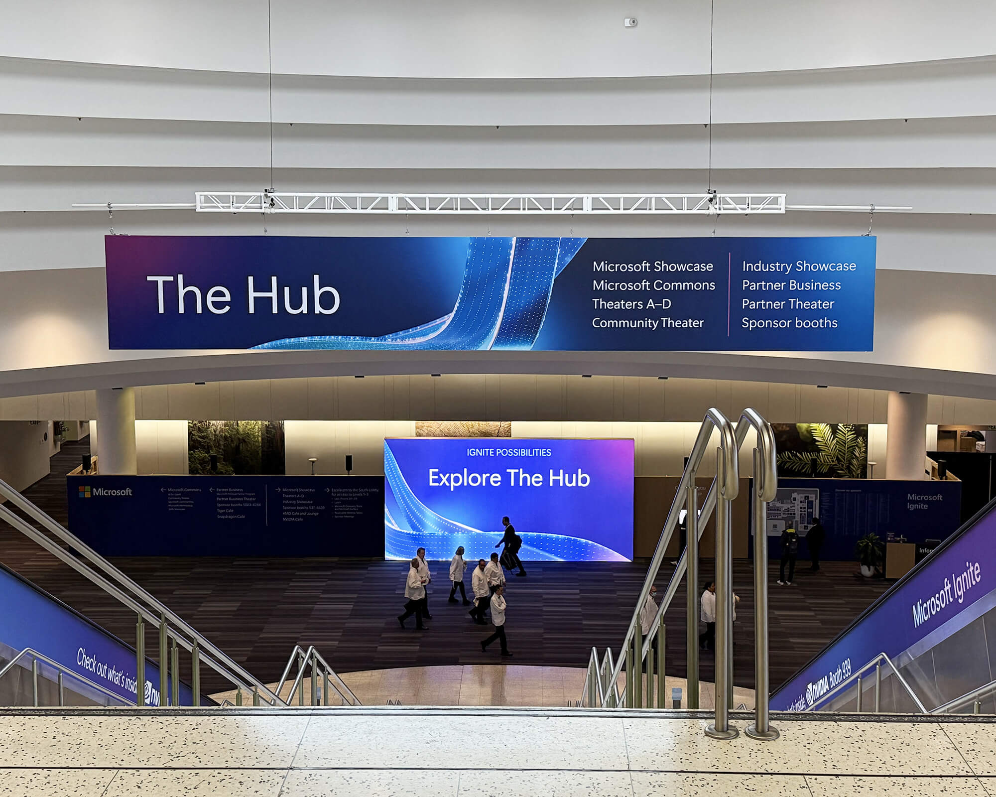 Sustainable large-format hanging banner and wayfinding signage produced and installed by SuperGraphics for The Hub at Microsoft Ignite, featuring event directory and branded escalator wraps.