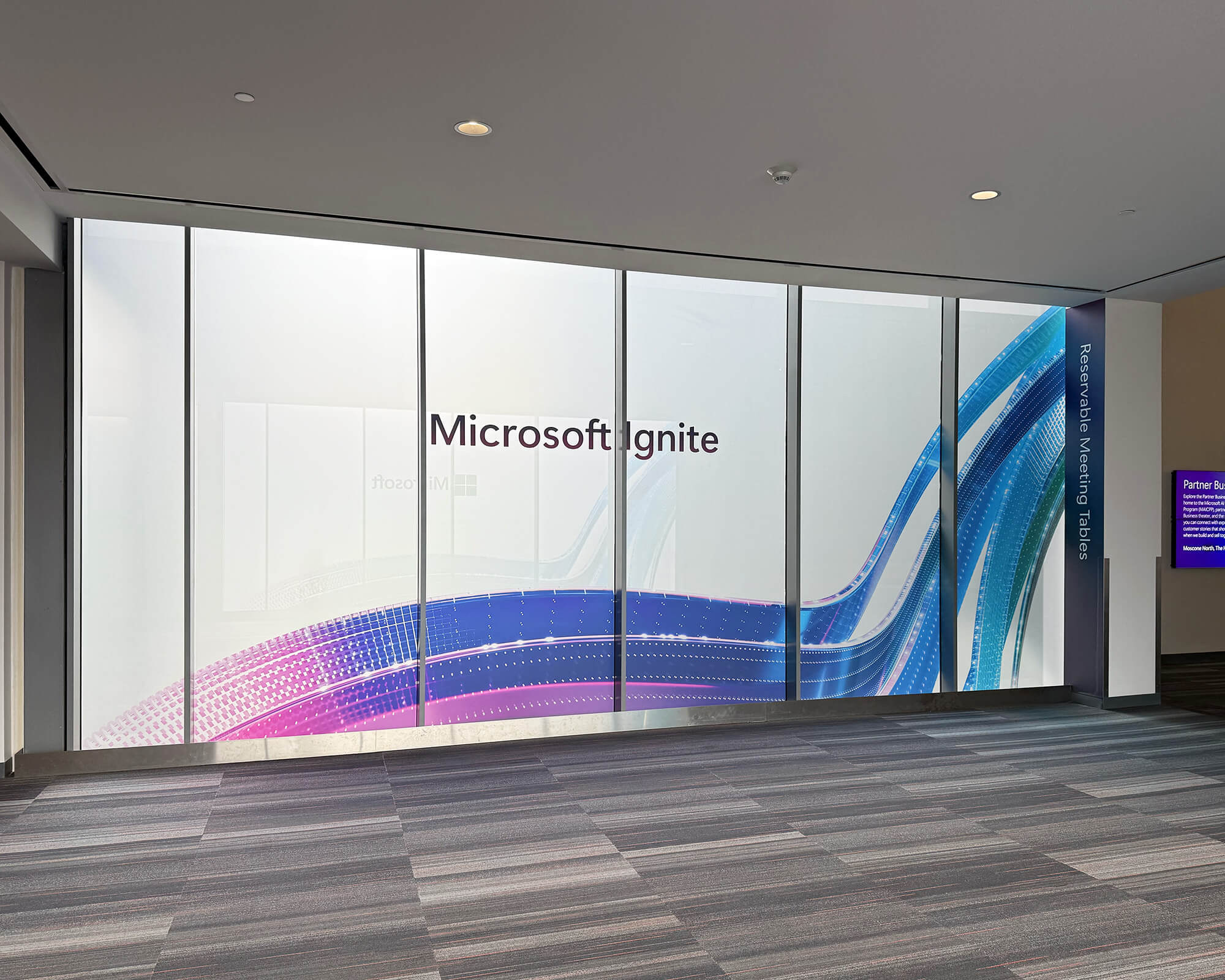 Sustainable large-format interior window graphics produced and installed by SuperGraphics for Microsoft Ignite, featuring frosted glass with colorful abstract wave branding in blues, purples, and pinks.