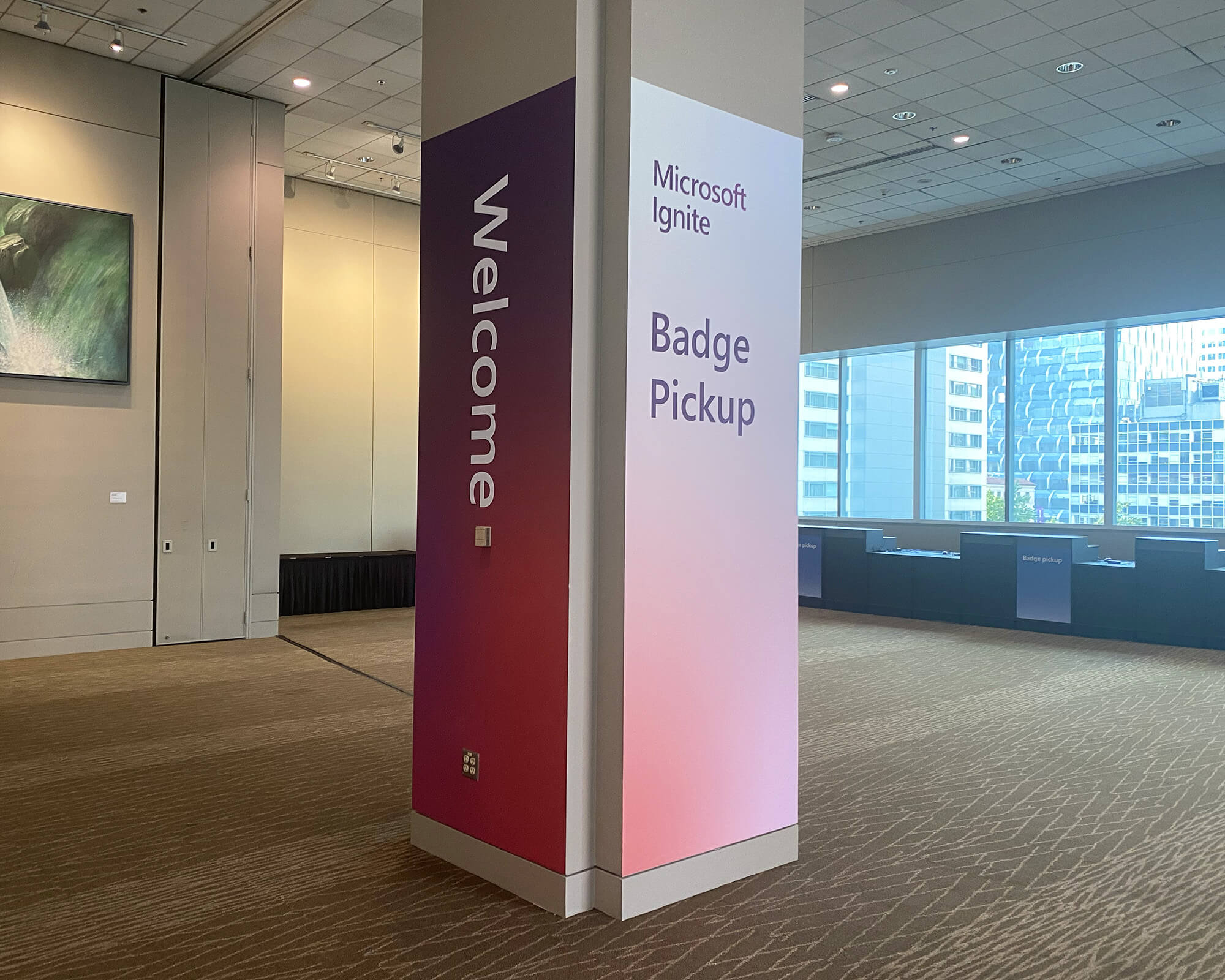 Sustainable branded column wrap produced and installed by SuperGraphics for Microsoft Ignite, featuring "Welcome" and "Badge Pickup" messaging with a deep red-to-pink gradient.