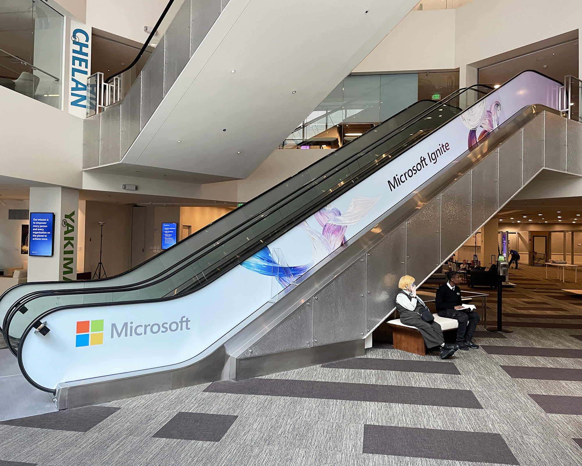 Sustainable branded escalator wrap produced and installed by SuperGraphics for Microsoft Ignite, featuring the Microsoft logo, event branding, and colorful abstract wave graphics.