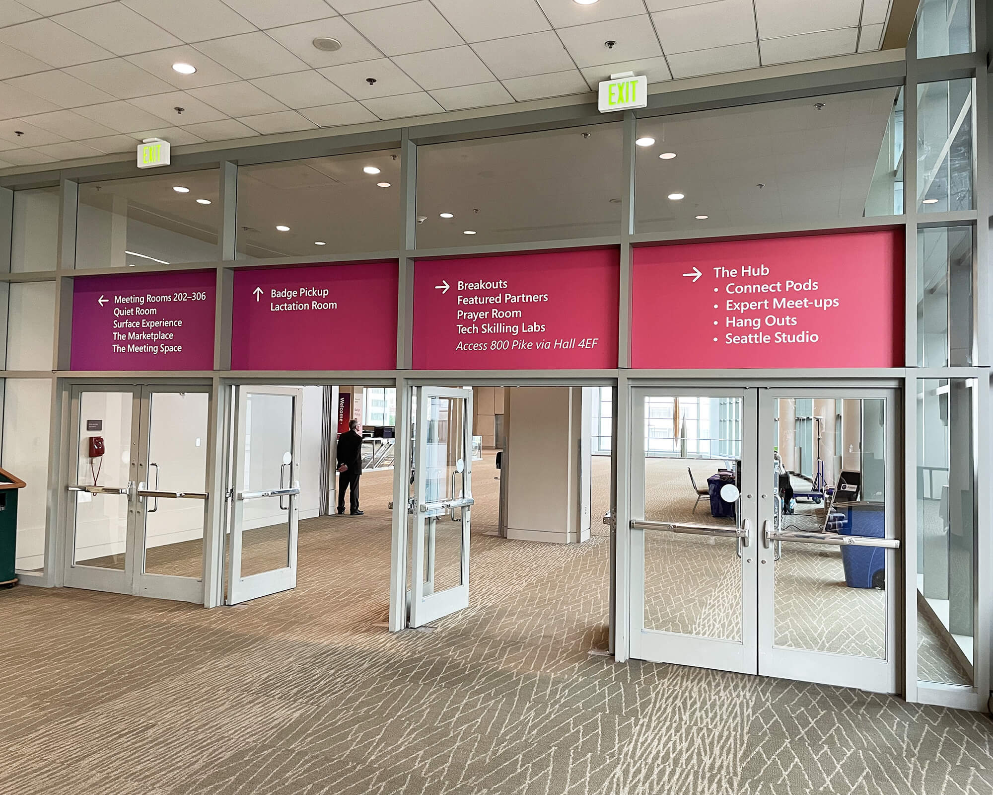 Sustainable overhead wayfinding window graphics produced and installed by SuperGraphics for Microsoft Ignite, featuring directional signage in bold pink panels above convention center doorways.