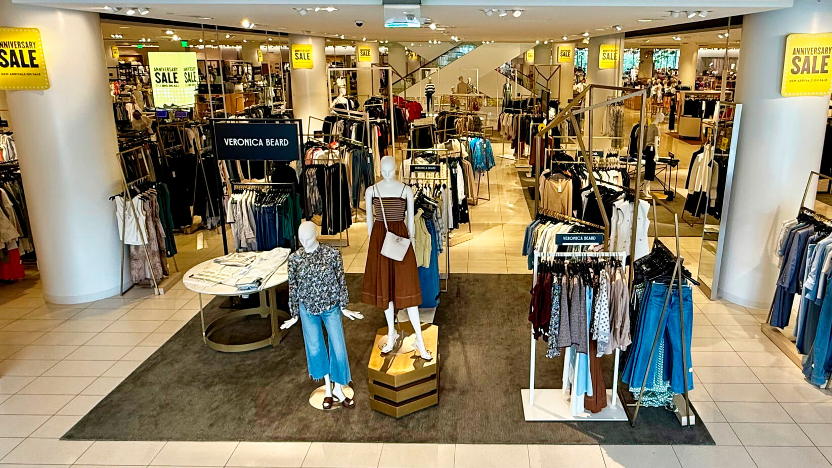 Nordstrom store interior during Anniversary Sale showing visual merchandising displays, styled mannequins, and yellow sale signage printed on sustainable substrates throughout the department.