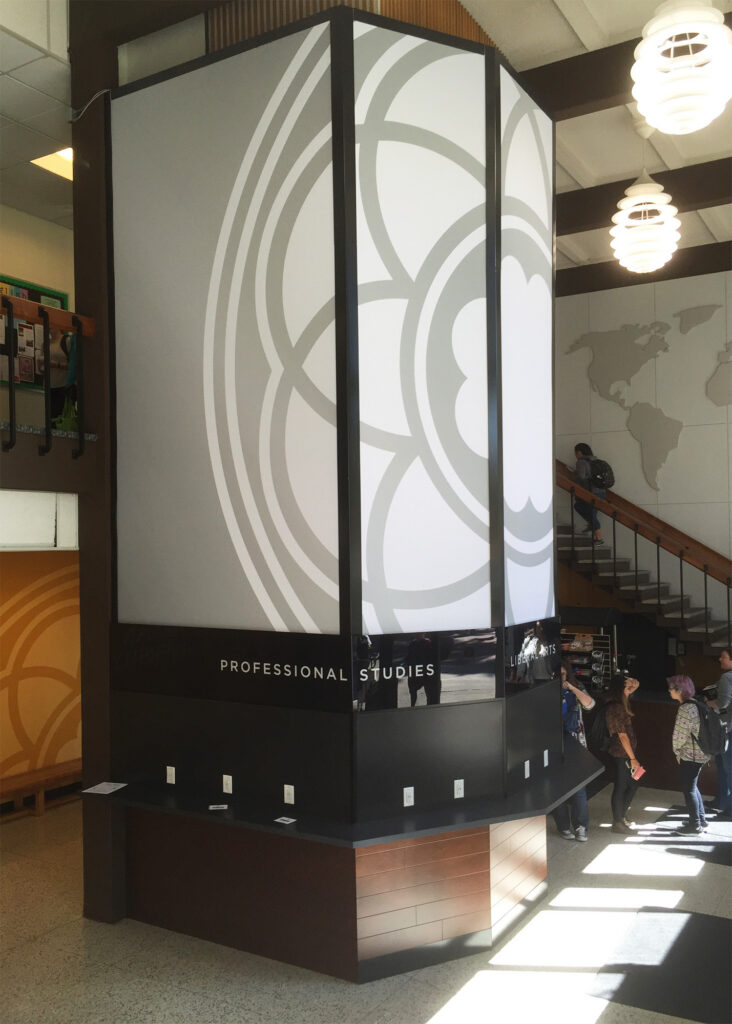 Illuminated multi-panel wayfinding kiosk in PLU's campus lobby featuring the university's medallion graphic and "Professional Studies" and "Liberal Arts" department labels, designed and produced by SuperGraphics.