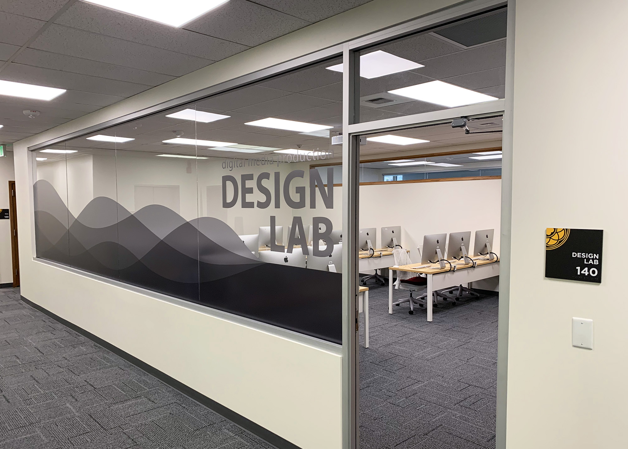 PLU Design Lab 140 with frosted glass wall graphics featuring wave patterns and "Design Lab" lettering, plus a branded room ID sign, produced by SuperGraphics.