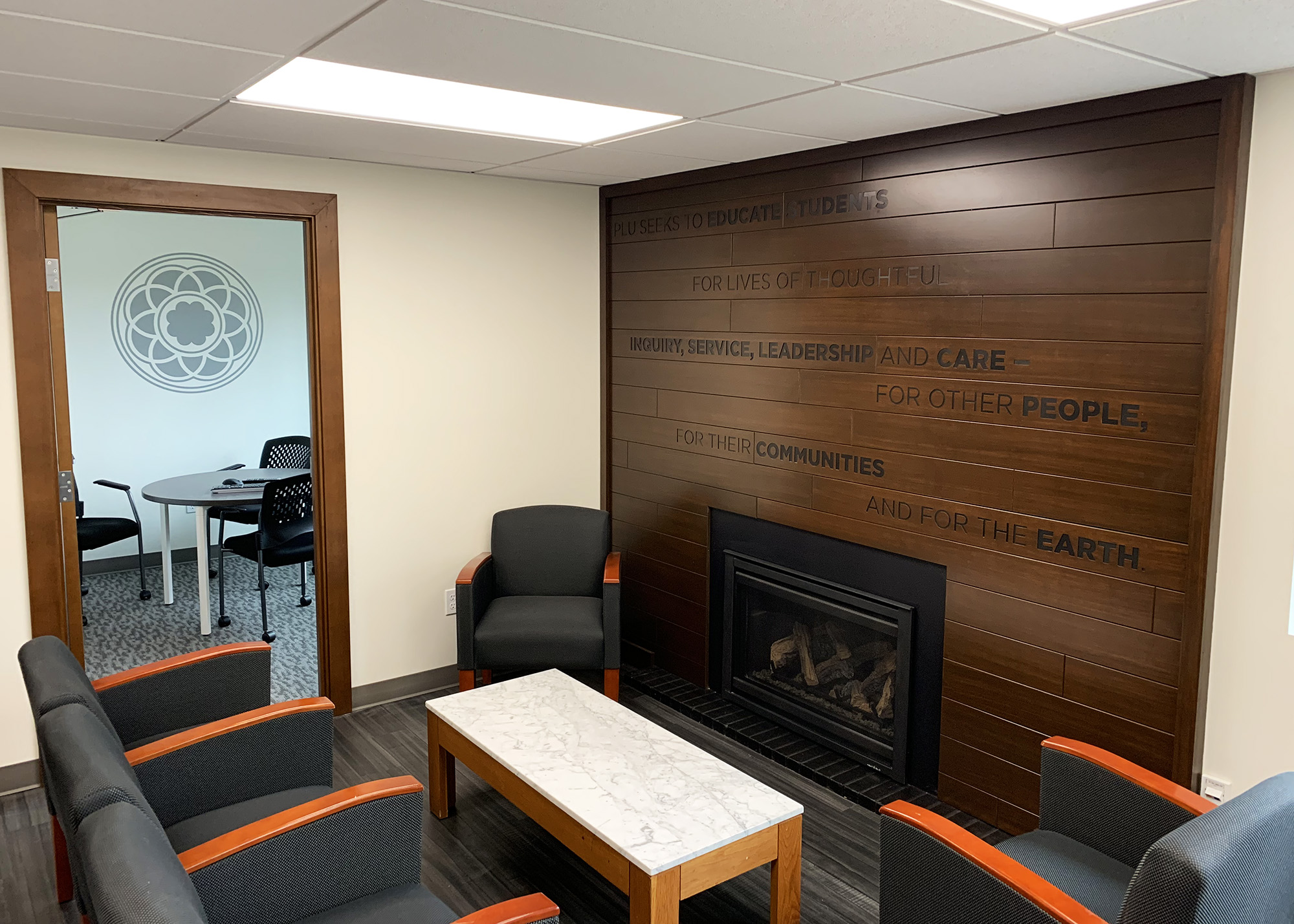 PLU campus lounge featuring a wood plank accent wall with the university's mission statement in dimensional lettering and a fireplace, produced by SuperGraphics.
