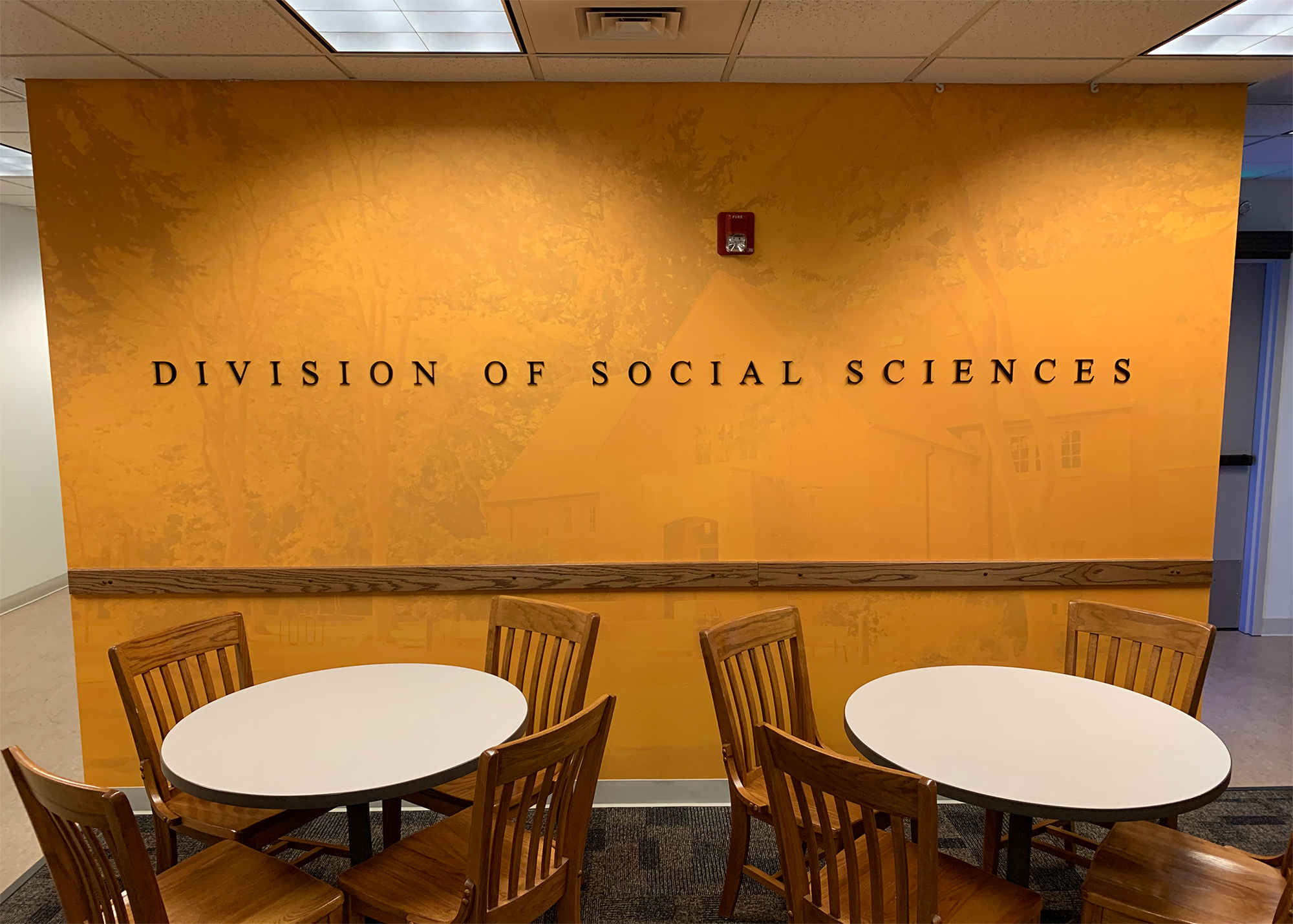 PLU Division of Social Sciences lounge featuring a warm gold wall mural with a subtle campus illustration and dimensional "Division of Social Sciences" lettering, produced by SuperGraphics.