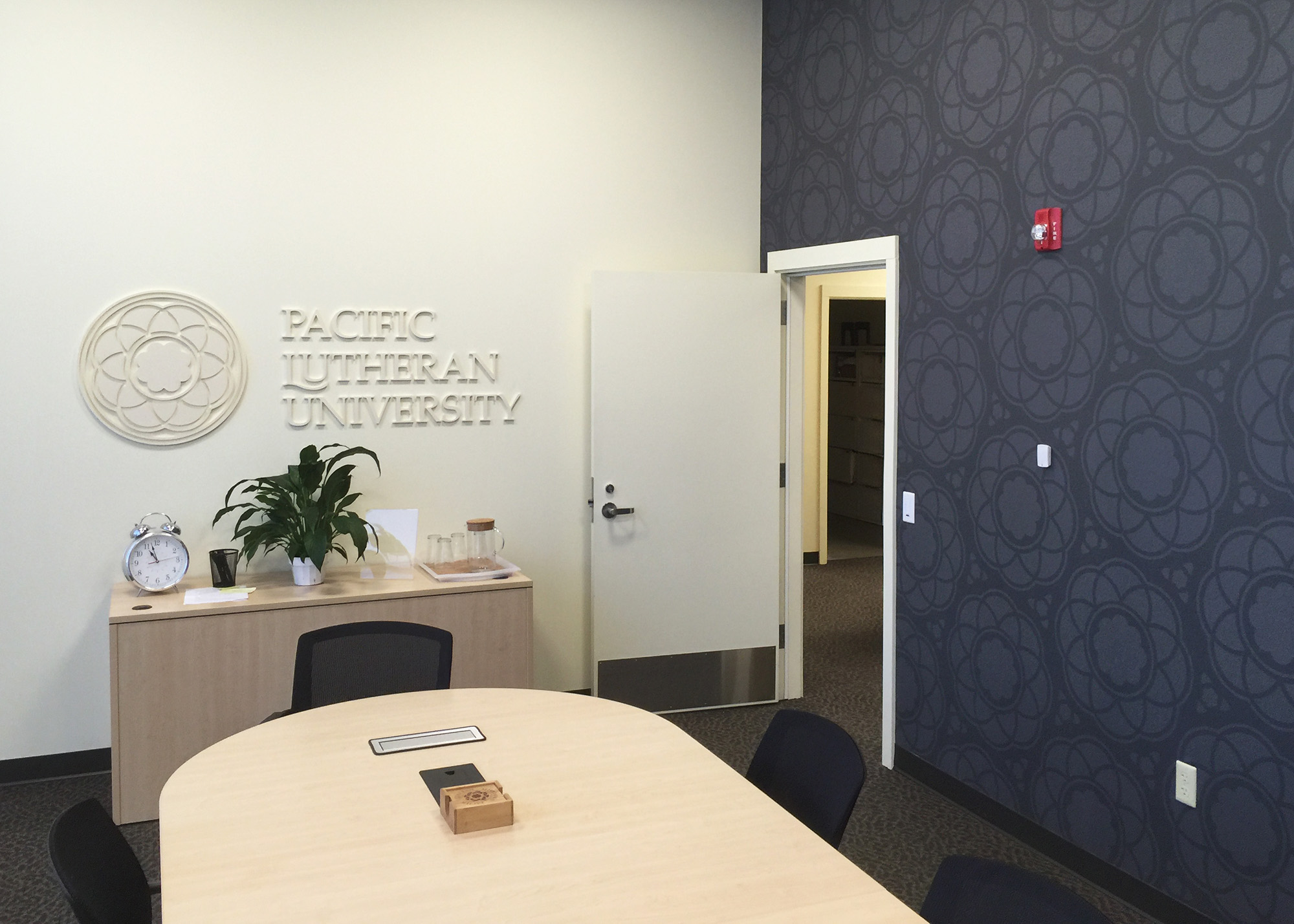 Pacific Lutheran University conference room featuring dimensional white logo and wordmark on a white wall alongside a dark navy medallion-patterned accent wall, produced by SuperGraphics.
