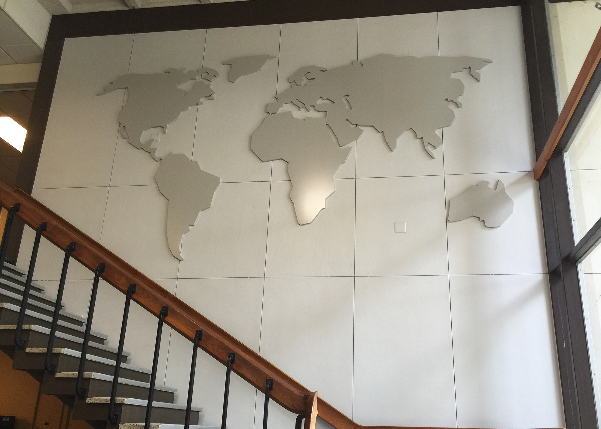 Large dimensional world map installation mounted on a white panel wall in a PLU campus stairwell, produced by SuperGraphics.