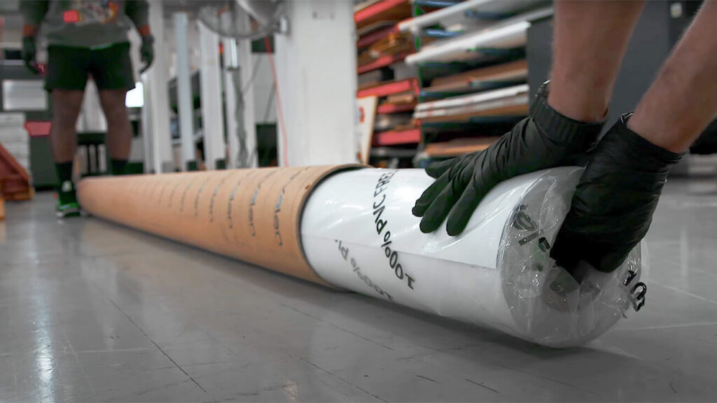A production team member wearing black gloves handles a roll of sustainable banner material on the shop floor.