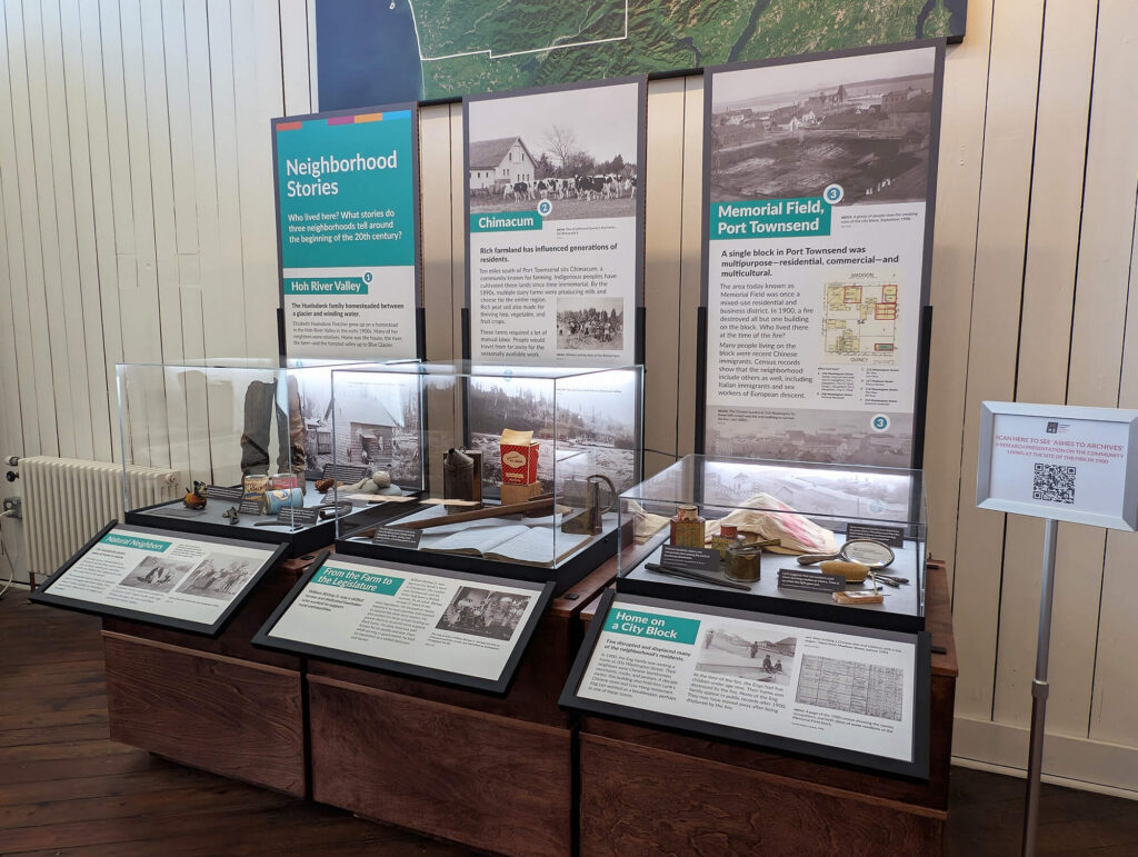 Modular exhibit panels and display cases at the JCHS Museum of Art + History showing the Neighborhood Stories exhibit, with interchangeable reader rails and standardized graphic panels exploring Hoh River Valley, Chimacum, and Memorial Field.