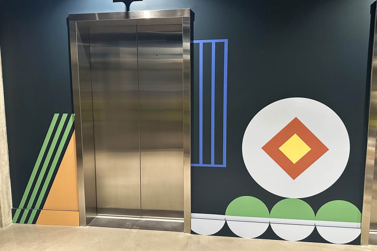 Colorful geometric wall graphics surrounding an elevator, featuring bold shapes, stripes, and circular patterns on a dark background.