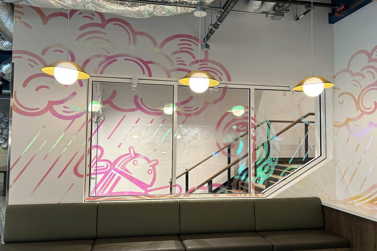 Colorful line-art mural with clouds and a whimsical character, applied to a stairwell wall and glass panels in a modern office space.