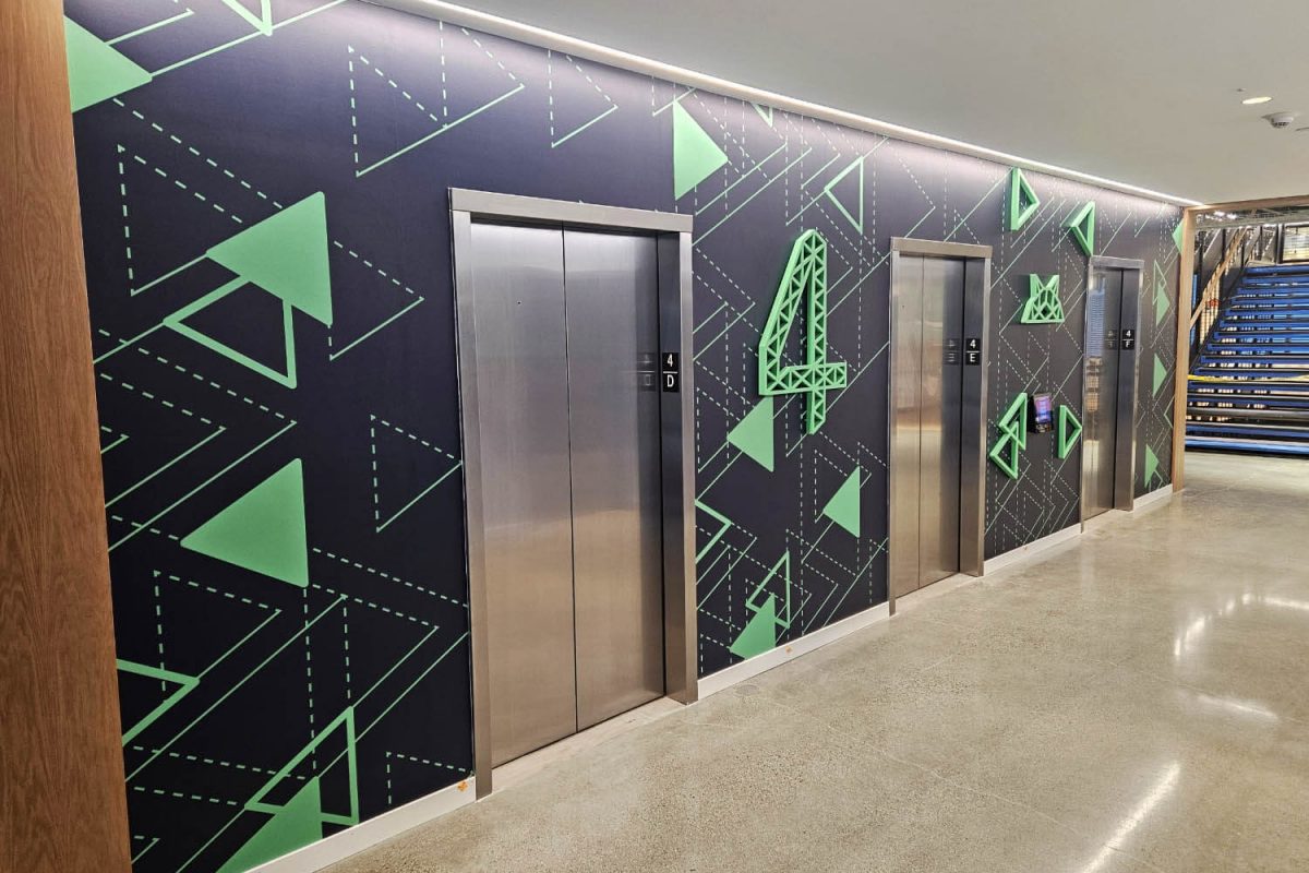 Elevator bay with a dark geometric wall mural featuring green triangles and dimensional number four markers.