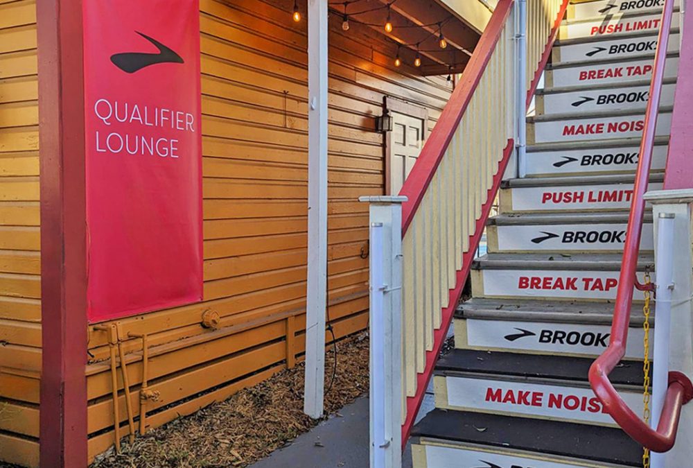 A staircase leading up to a deck, with custom graphics on the stairs and a banner for the Brooks Qualifier Lounge.