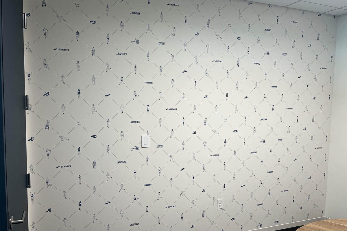 Patterned wall featuring repeating line-art runner illustrations and Brooks branding inside a modern office room.