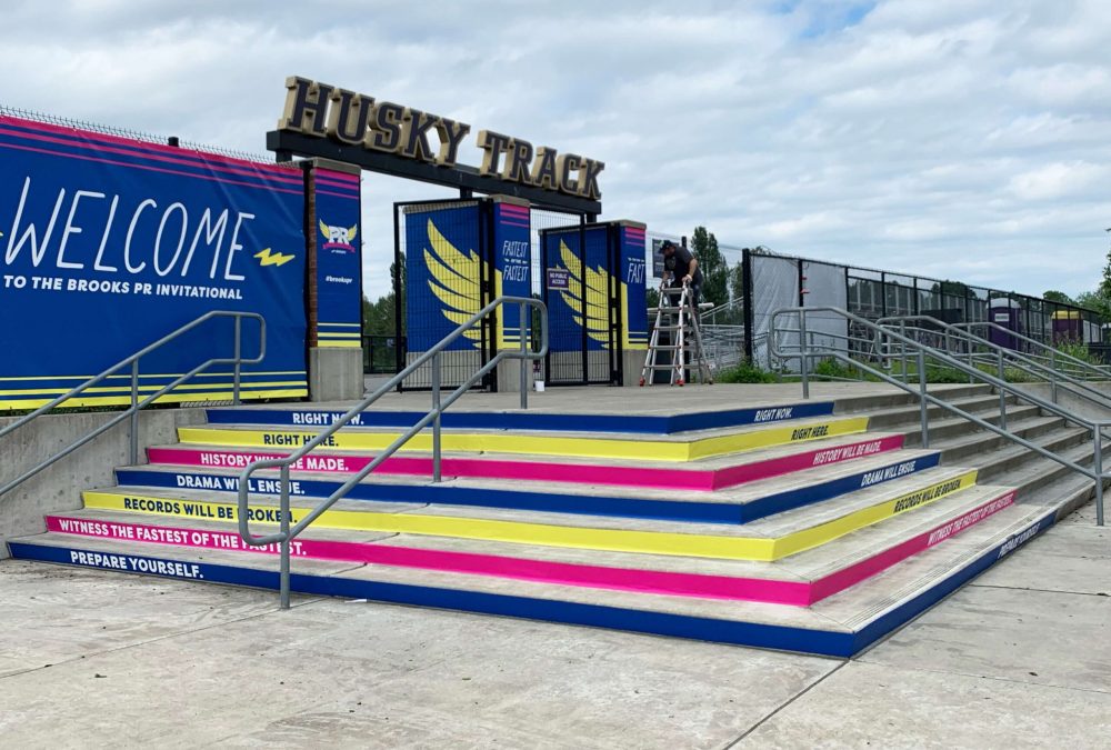 Stair riser graphics for Brooks' PR Invitational event, produced and installed by SuperGraphics. Showcases blue, pink, and yellow strips up a staircase with motivational messaging.