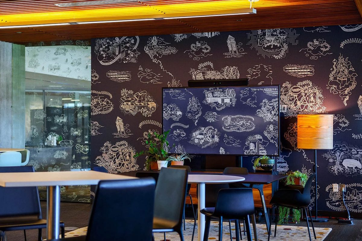 Dark wall mural featuring white hand-drawn illustrations of buildings, landscapes, and whimsical scenes in a modern office café area.