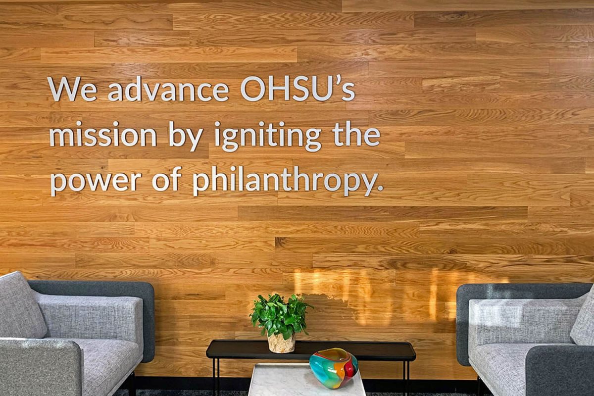 Dimensional mission statement lettering mounted on a wood-paneled wall in a modern office seating area.