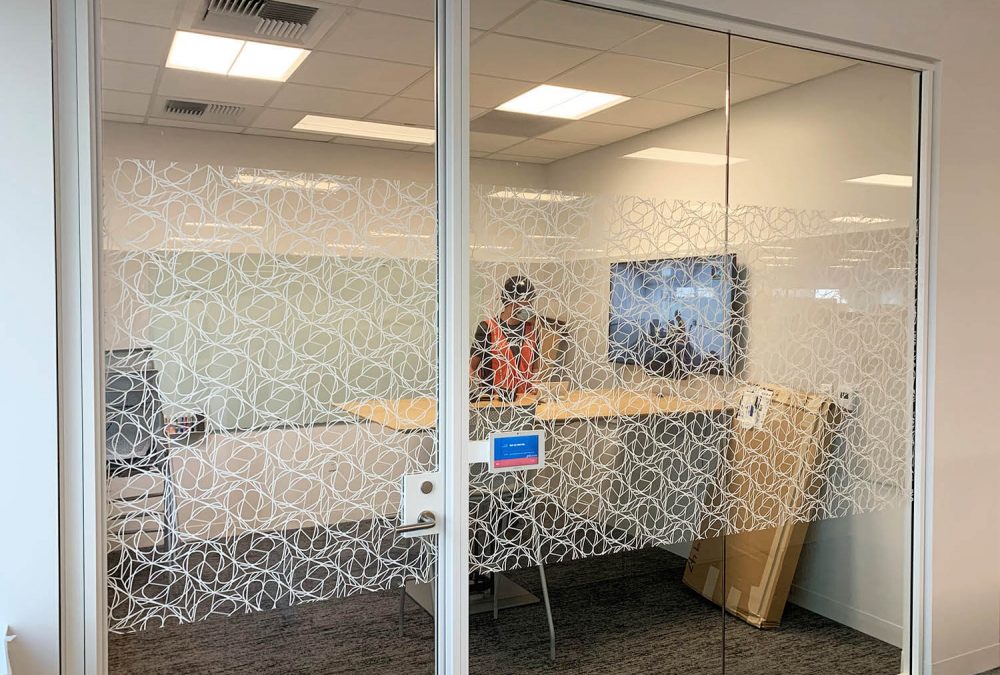 Conference room storefront with white patterned frosted glass graphics providing partial privacy in a modern office.